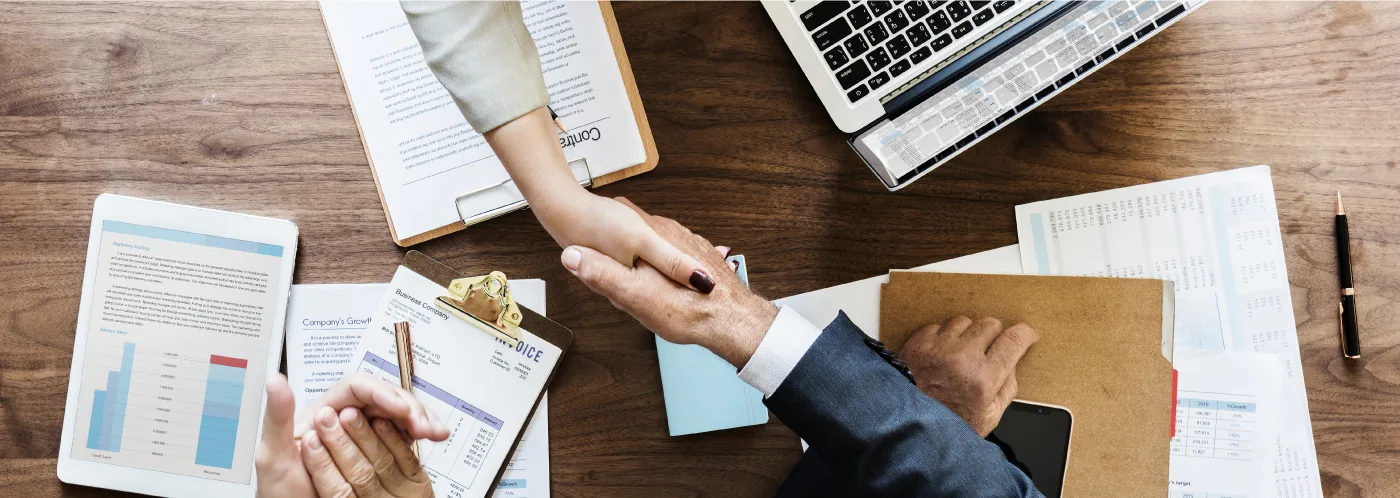 Aperto de mãos sobre uma mesa com contrato, relatórios e notebook